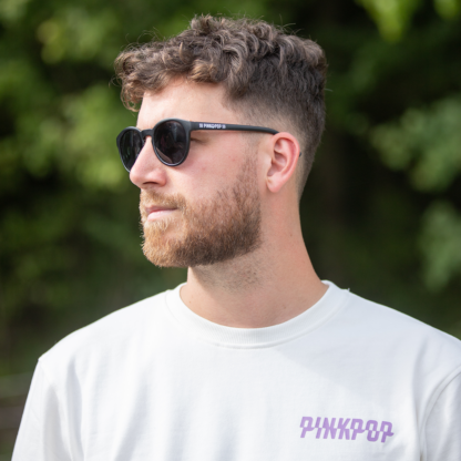 Man met zwarte zonnebril met wit Pinkpop-logo op zijkant oortje.